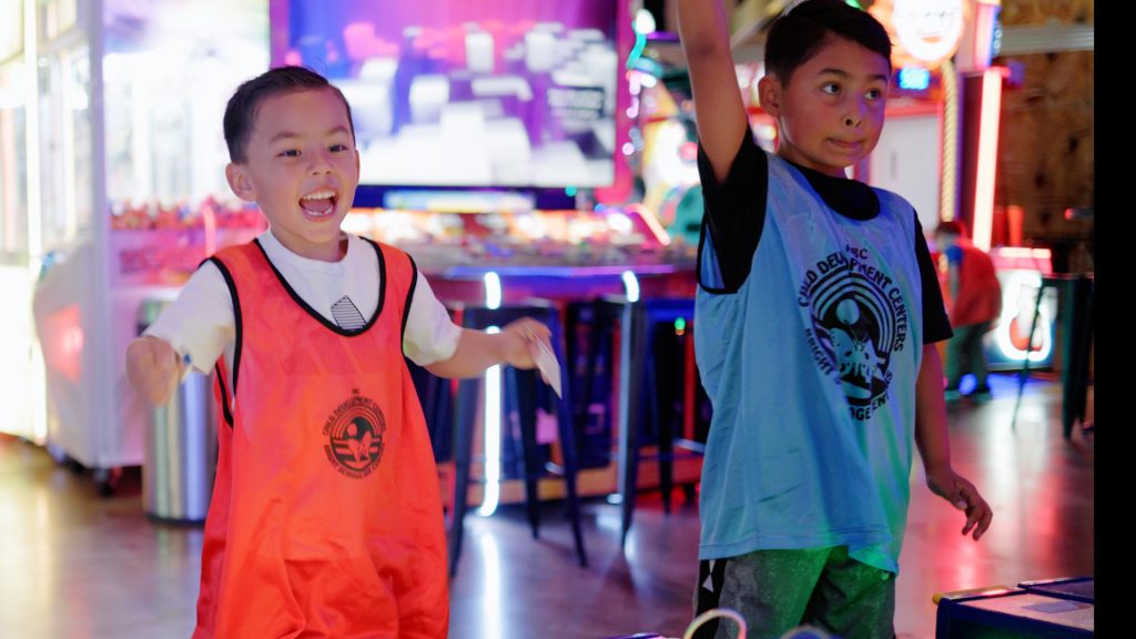 Two school-age children wearing ABC Child Development Centers vests celebrating at an arcade during an after-school field trip in Windsor, Colorado