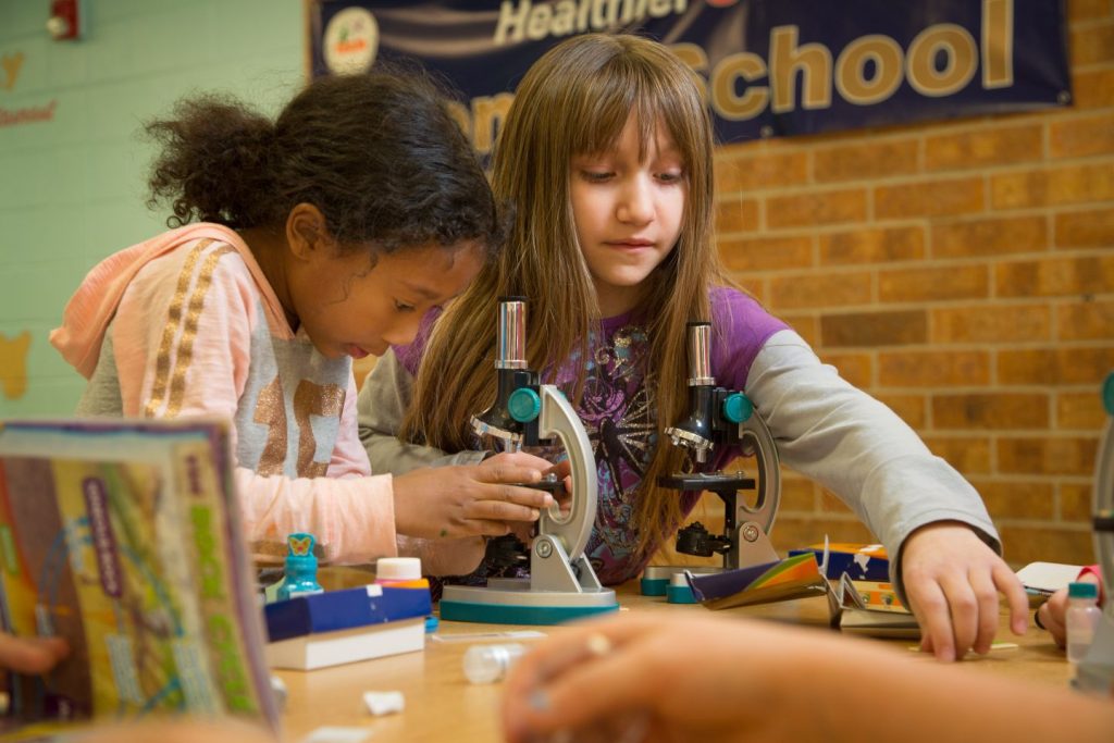 Two school-age girls working together with microscopes during a hands-on science activity at an after-school program in Greeley